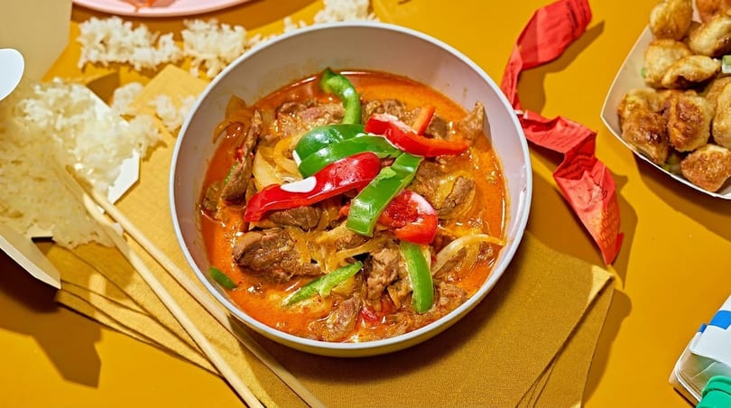 Red curry with beef, bell peppers, and onions, served with rice and dumplings.
